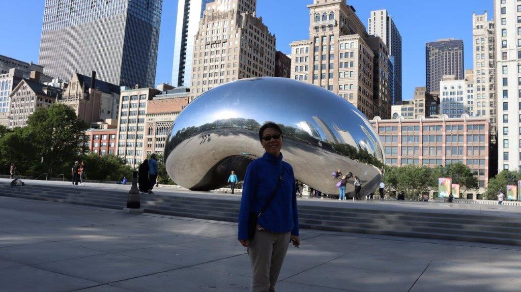 A person standing in front of a large silver object with Millennium Park in the background

Description automatically generated