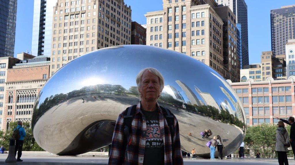 A person standing in front of a reflective object with Millennium Park in the background

Description automatically generated