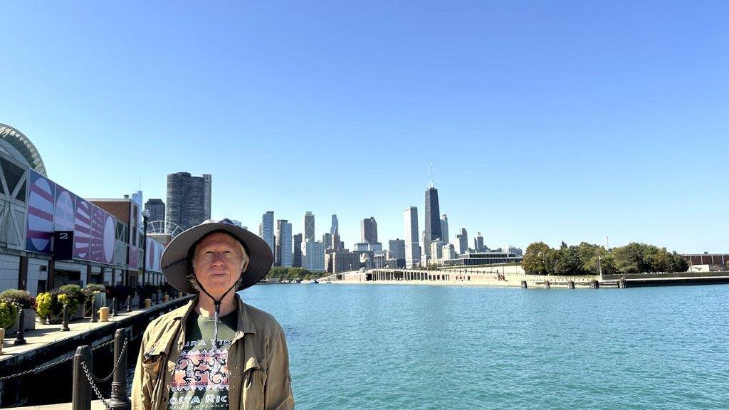 A person standing in front of a body of water with a city in the background

Description automatically generated