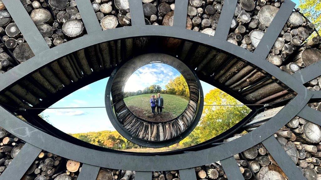 A reflection of a couple in a mirror in a hole in a wall

Description automatically generated