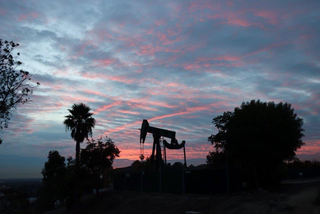 A silhouette of a pumpjack and trees

Description automatically generated