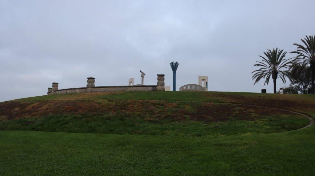 A grassy hill with a stone wall and a blue post

Description automatically generated