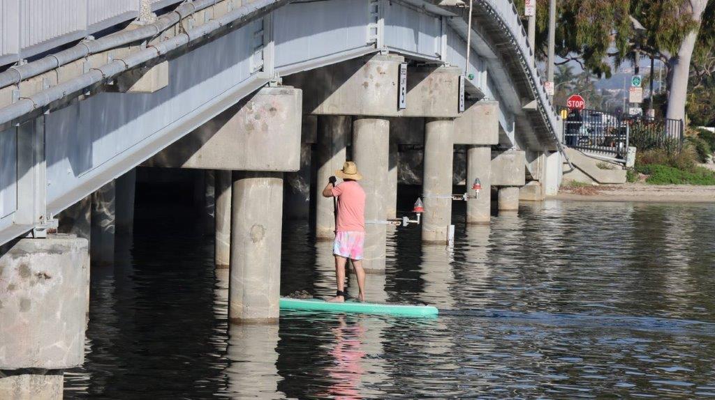 A person standing on a surfboard under a bridge

Description automatically generated