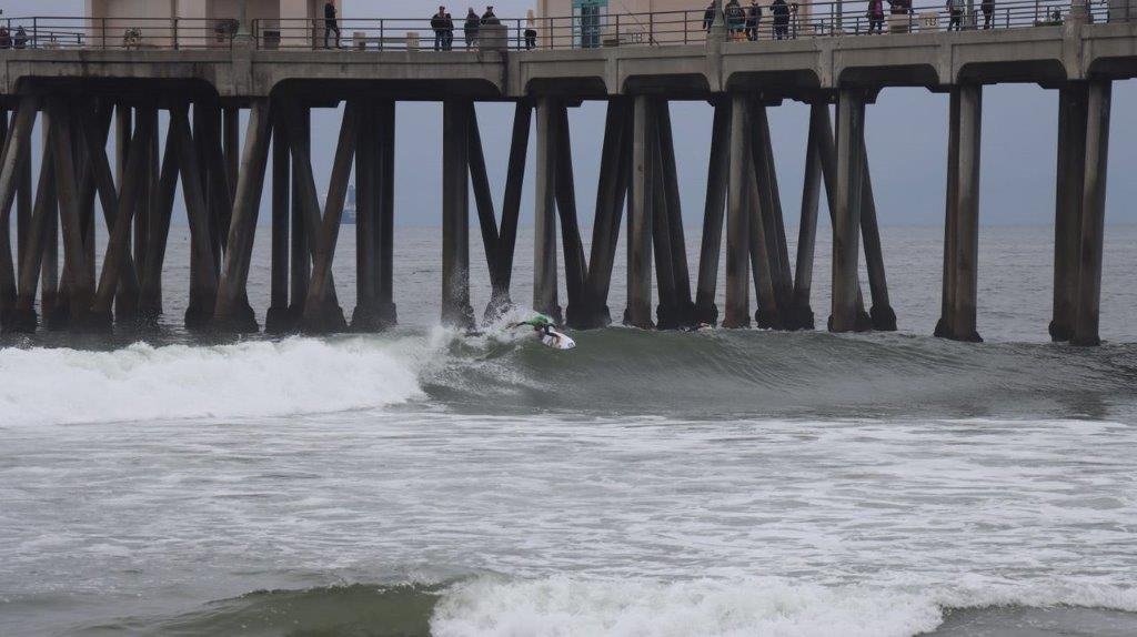 A surfer riding a wave under a pier

Description automatically generated